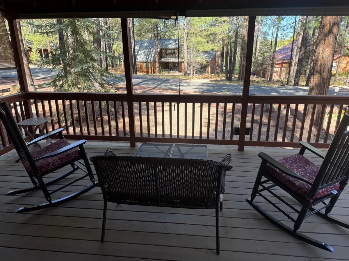 This image features a classic wrap-around porch with several inviting rocking chairs set against a sturdy wooden railing. The porch overlooks a tranquil street lined with mature trees, and the dappled sunlight creates a restful, peaceful ambiance. The arrangement encourages moments of relaxation, perfect for sipping coffee or enjoying the gentle sounds of nature.