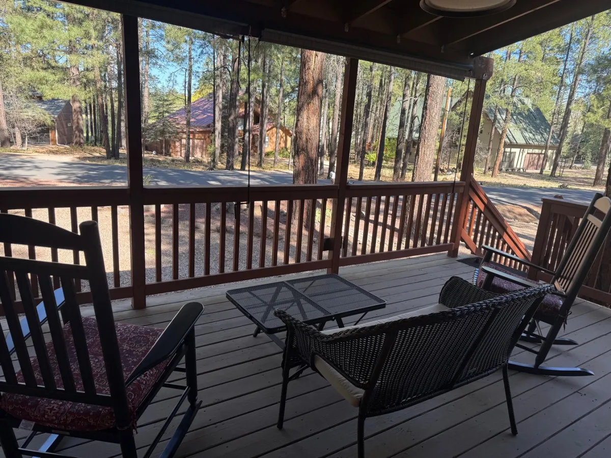 An inviting porch with a rocking chair and table is surrounded by trees, offering views of seasonal foliage and glimpses of wildlife. The space is ideal for relaxing after a day of outdoor adventure or enjoying the changing light at sunset.