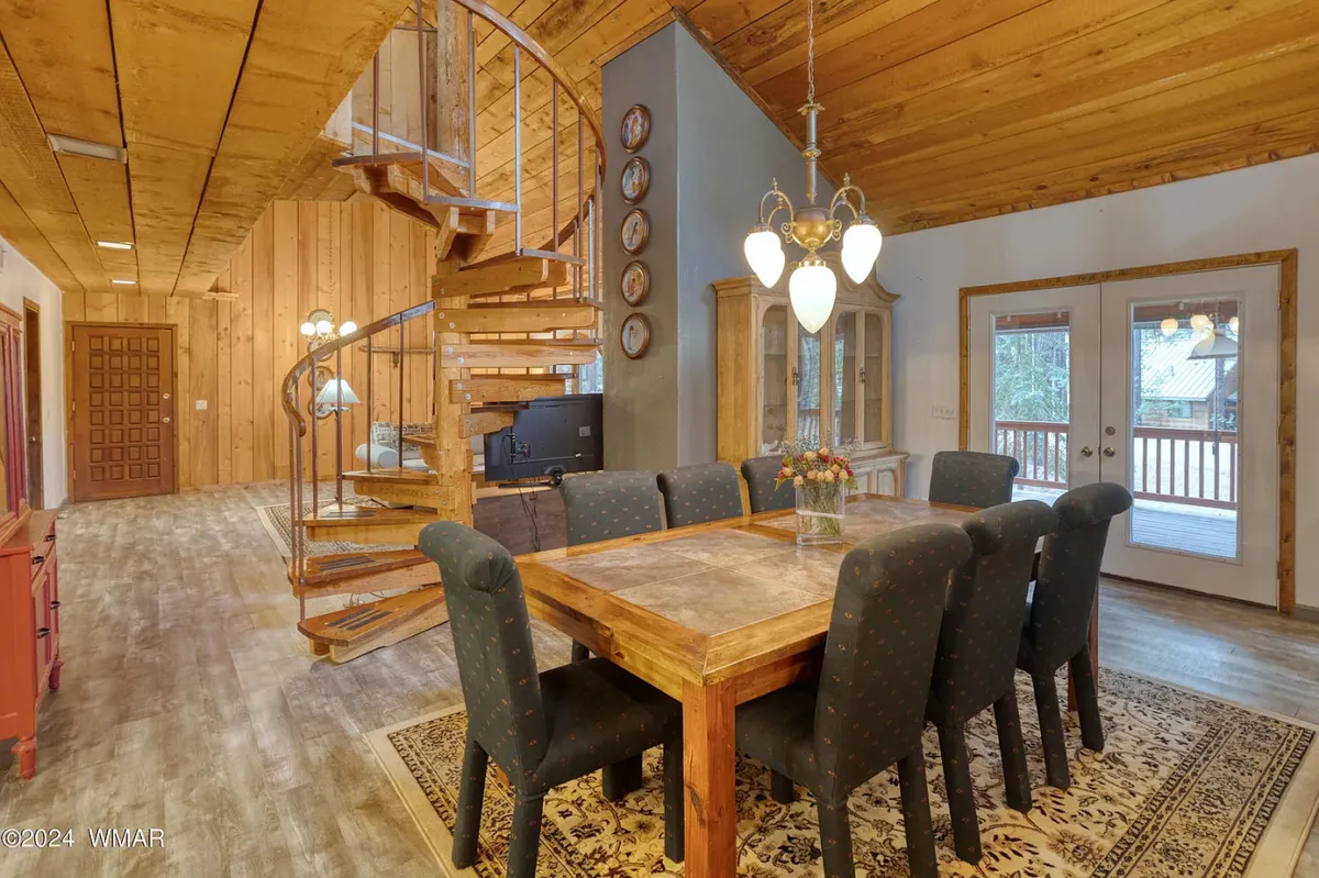 A cozy dining area featuring a large table set beneath a window, with a spiral staircase adding architectural interest. The scene is bathed in natural light, and the table is clearly the centerpiece for group meals and celebrations. A door nearby hints at easy access to the outdoors.